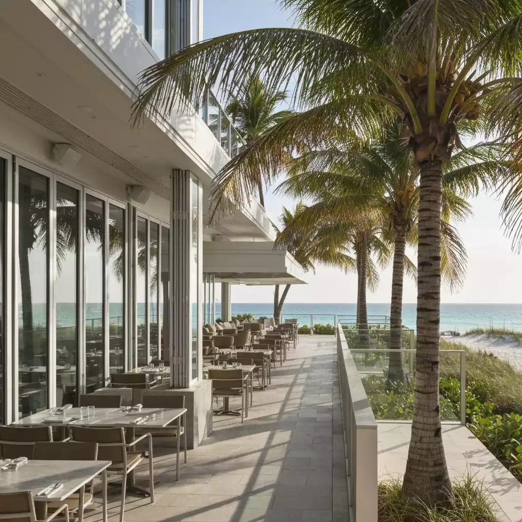 Modern restaurant exterior with outdoor seating overlooking Fort Myers Beach, sunny day, palm trees